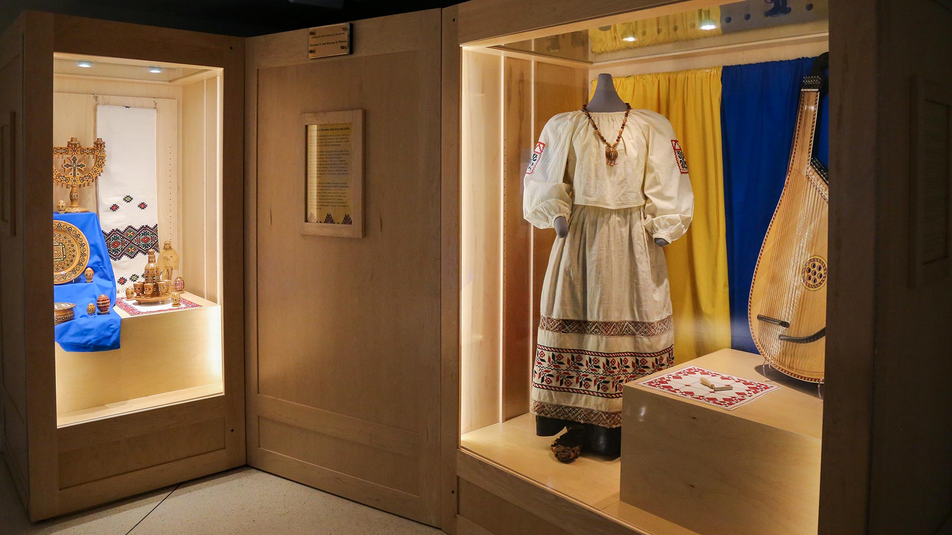 overview of exhibit with a case of woooden eggs and other objects on left and a dress on right