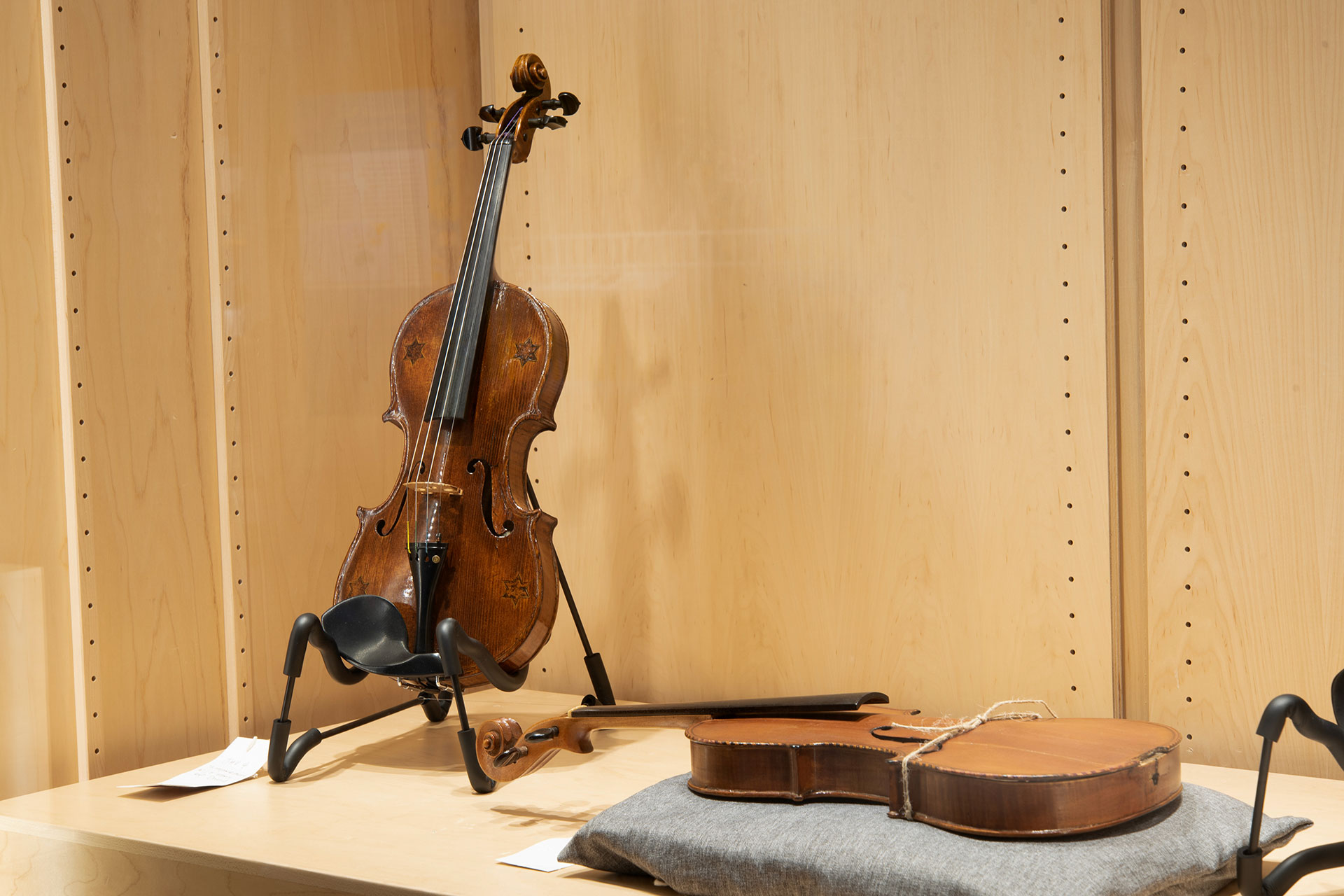 A brown violin displayed vertically on a stanc and a light brown violin displayed horizontally