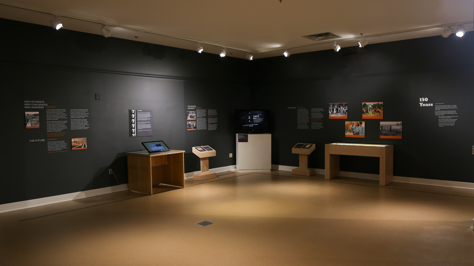 overview shot of another part of the exhibit, with more text, text panels, and pictures on the walls and electronic devices on display to interact with