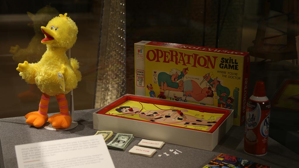 shot of objects in a case containing the 'operation' game, big bird from 'sesame street' and a can of 'reddi wip'