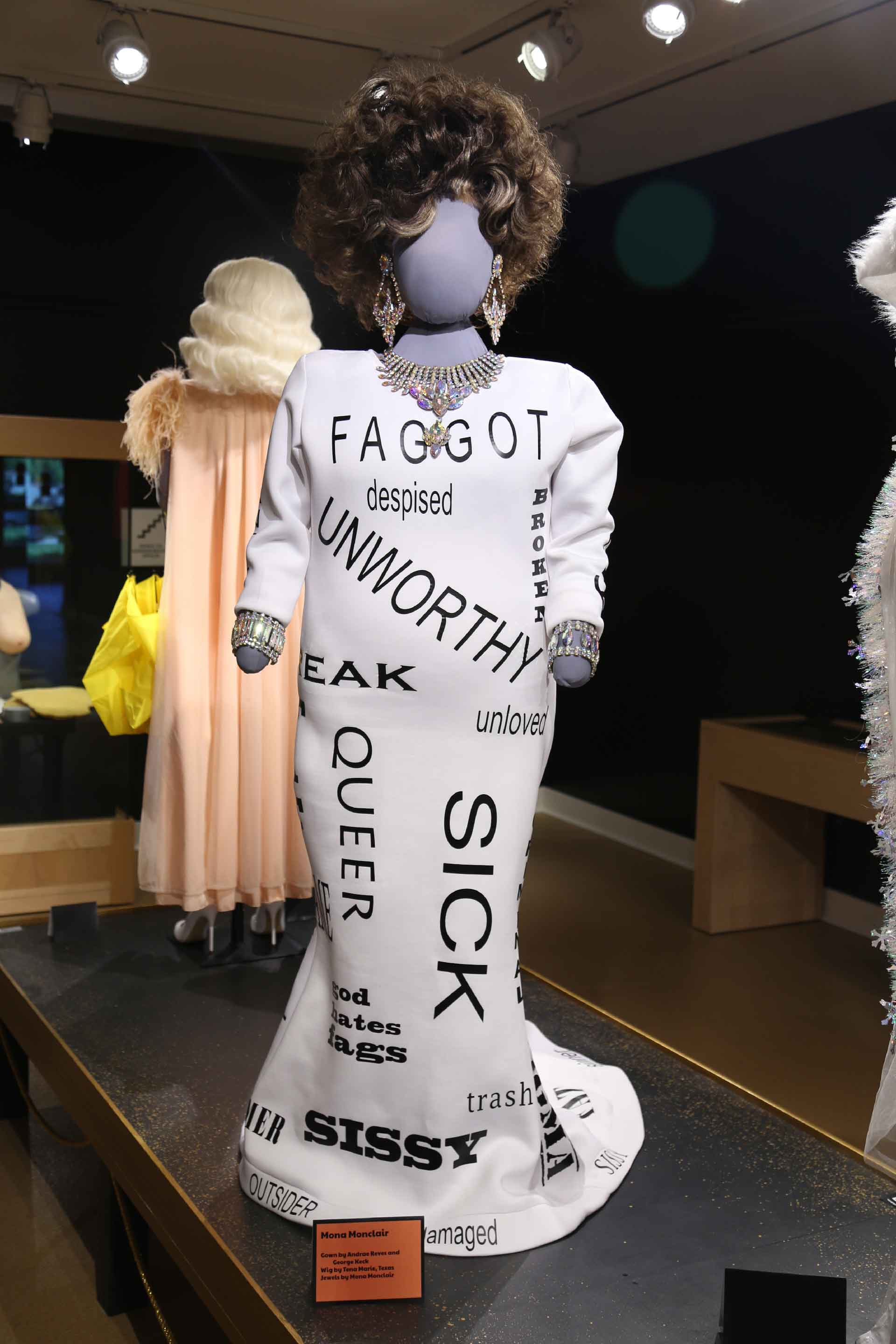 Drag queen dressed in white dress with black text on it