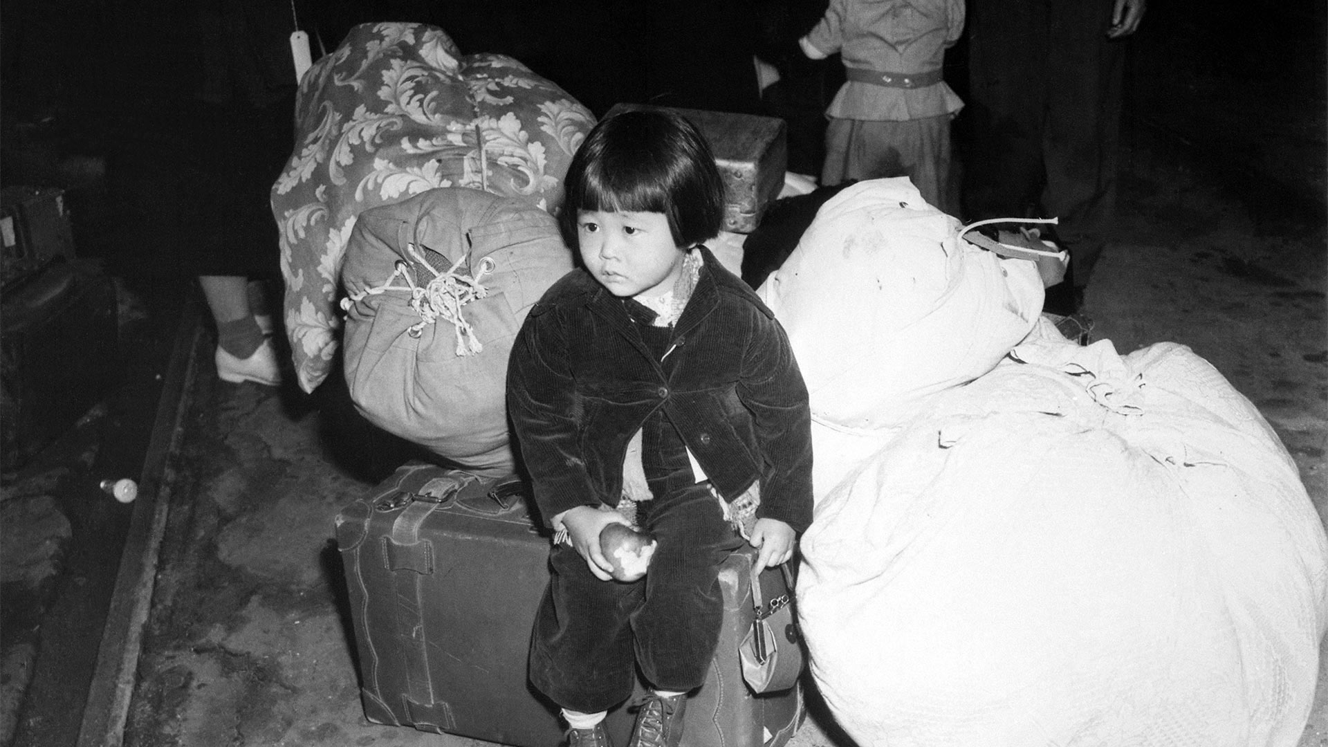 black and white photo of very young Japanese girl waiting with luggage on train platform