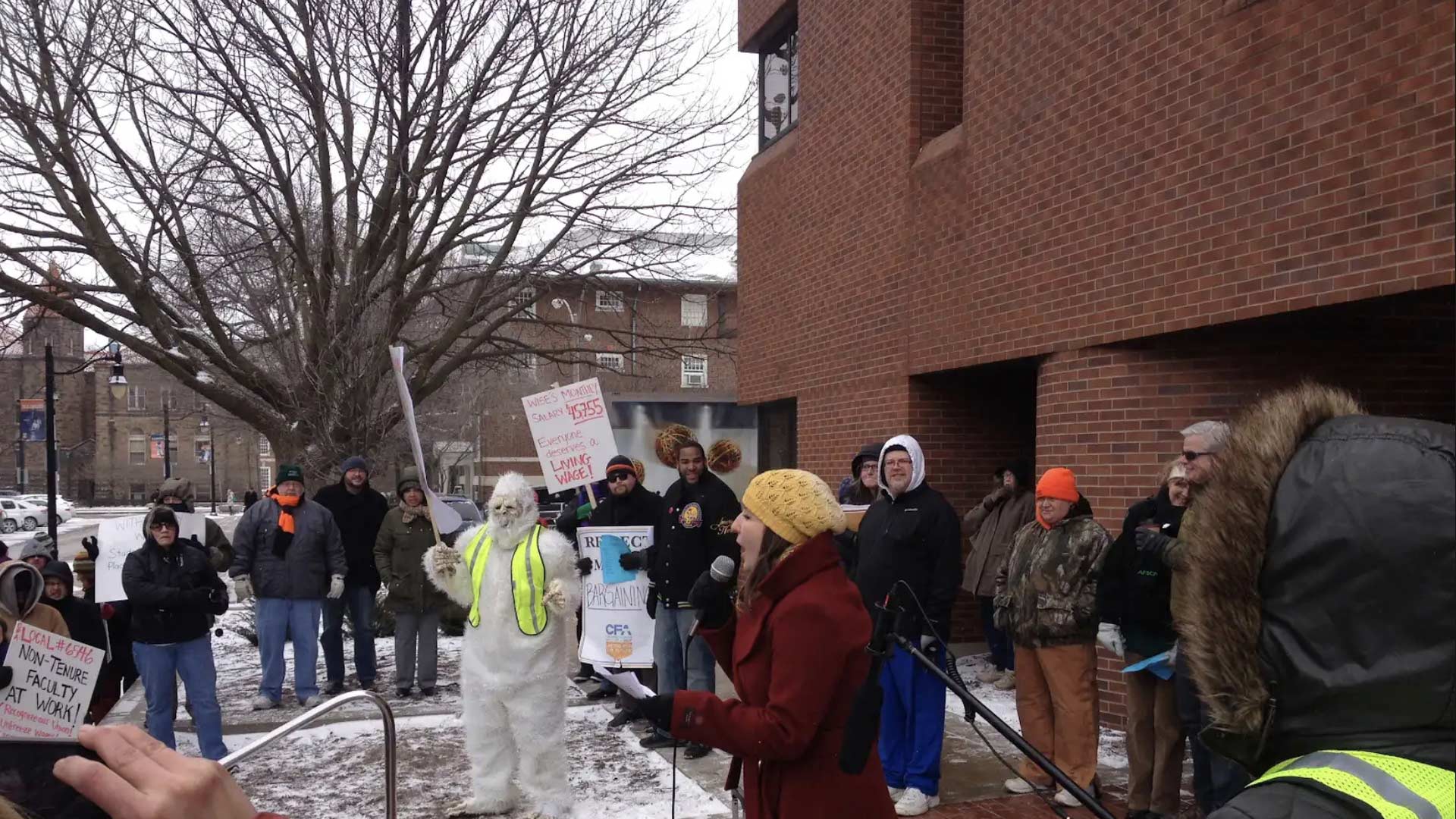 Group of community members holding signs surrounding a person in a yeti costume
