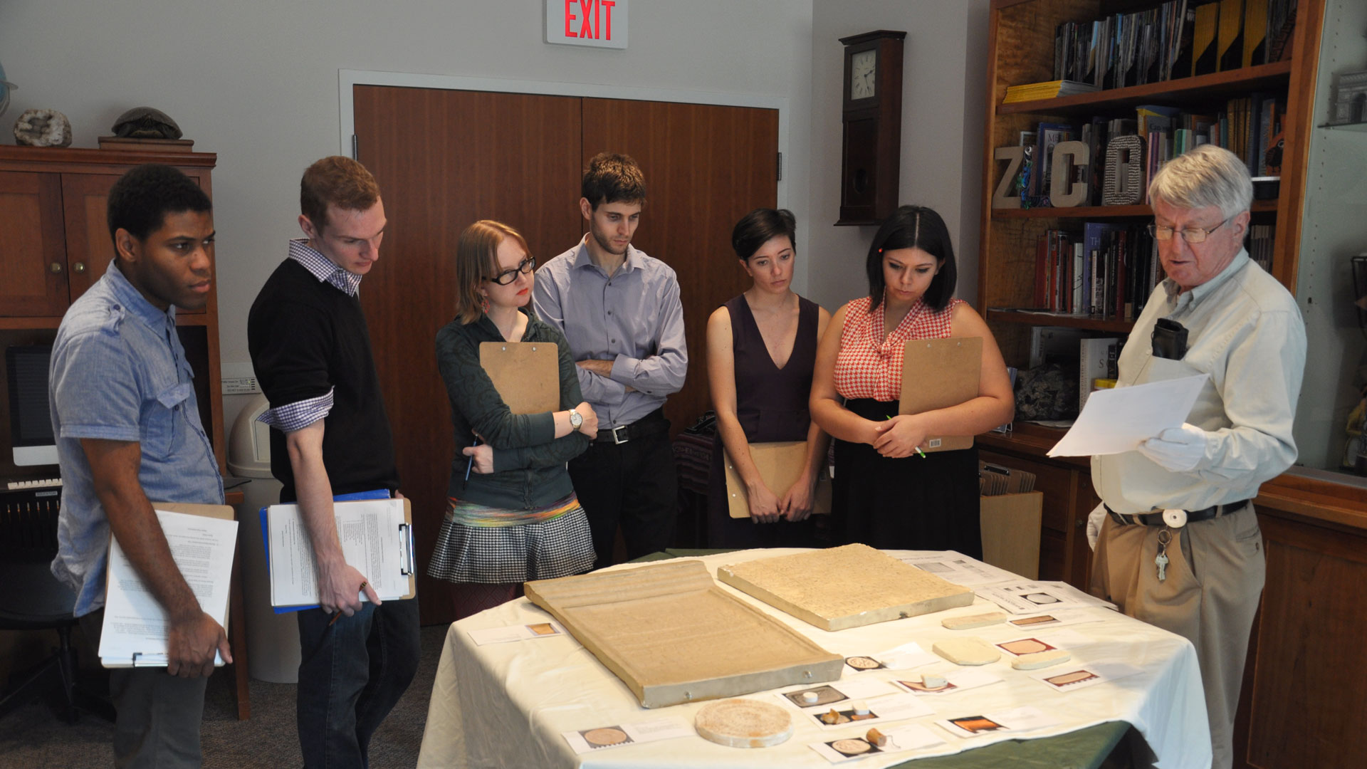 group of university students looking at an object a professor is holding